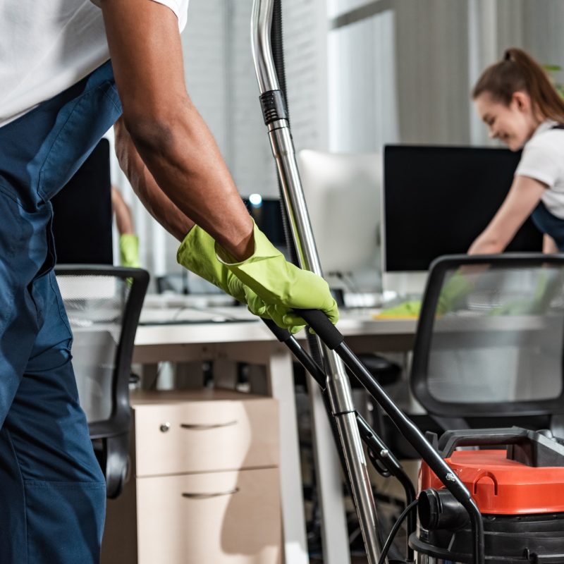 cropped view of african american cleaner moving vacuum cleaner in office