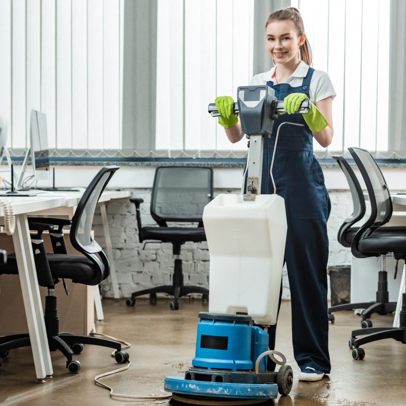 smiling cleaner washing floor in office with cleaning machine